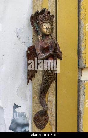 Small bronze sculpture of mermaid godess, made in the shape of door handle and attached to the wall or the yellow door, viewed in close-up. Stock Photo
