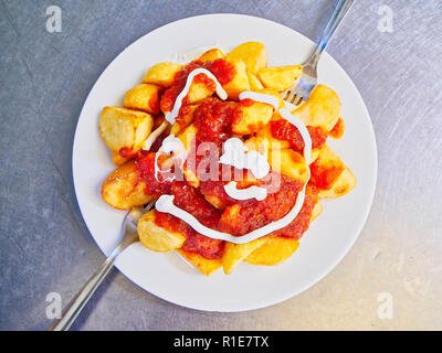 A portion of Patatas Bravas over a metallic table. Fried potatoes topped with spicy sauce, one of the most common typical Spanish tapas. Stock Photo