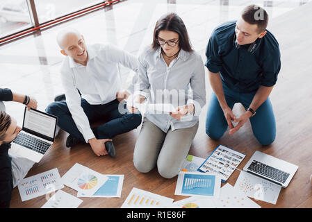 Planning strategy together. Business team looking at papers on floor with manager pointing to one idea. Cooperation corporate achievement. Planning design draw. Teamwork concept Stock Photo