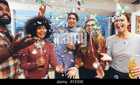 Happy businessmen and women holding drinks having fun at a party. Friends having a get together party enjoying drinks with confetti flying around. Stock Photo