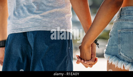 Rear view close up of hands of a romantic couple walking outdoors. Close up of man holding hand of a woman. Stock Photo