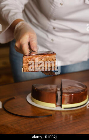 Prague mousse cake. Woman shows the filling and sponge cake. Mirror glaze glitters deliciously. Modern cooking. Cooking in a pastry shop. Stock Photo