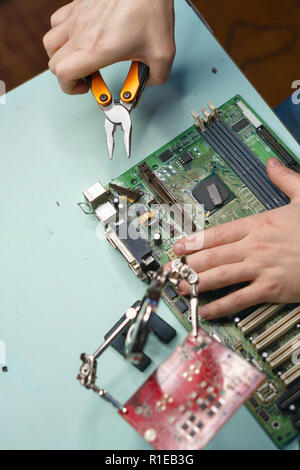 Repair motherboard. Man with pliers remove connector from the motherboard. Close-ups Stock Photo