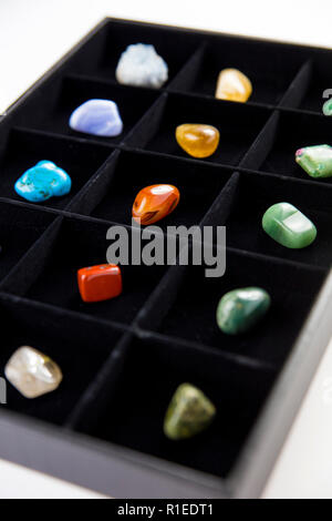 Variety of colorful semi precious stones crystals in organizer box sorted by color isolated on black. Stock Photo