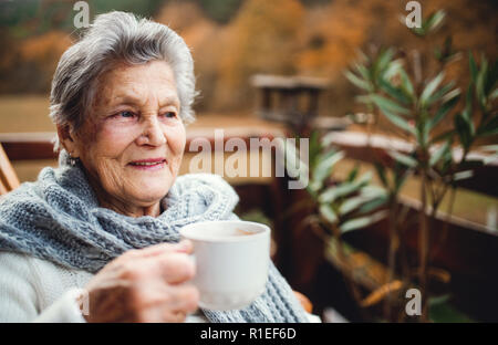 An elderly woman standing outdoors on a terrace on a sunny day in autumn. Stock Photo