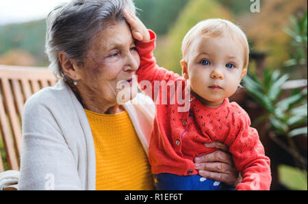 Elderly woman sitting with a toddler great-grandchild on a terrace in autumn. Stock Photo