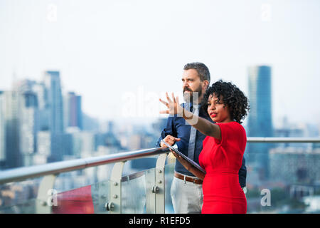 A portrait of two businesspeople standing against London view panorama, talking. Stock Photo