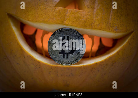 Bitcoin cryptocurrency physical coin placed inside the mouth of carved pumpkin Stock Photo