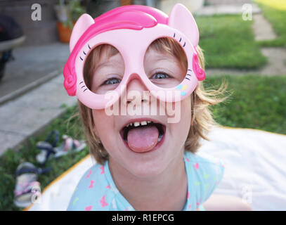 Little girl with a mask on her face is laughing and playing on the green lawn Stock Photo