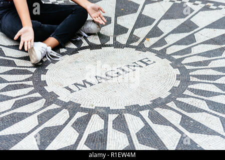 New York City, USA - June 23, 2018: Young woman sitting on the Imagine mosaic in the Strawberry Fields in Central Park. Stock Photo