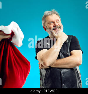 An elderly man with white hair and beard and Christmas gift bag. He getting ready for the role of Santa. Human emotions and holiday concept Stock Photo