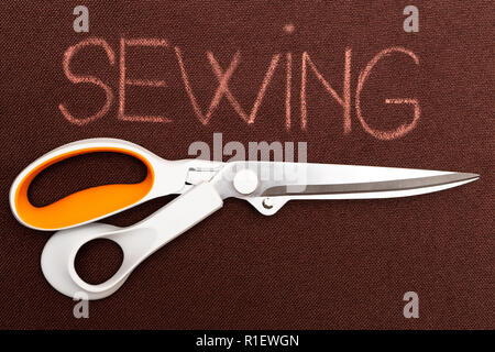 Sewing text on brown material background underlined with pair of scissors Stock Photo