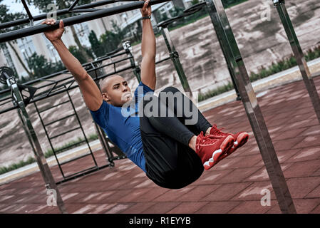African man is doing stretching exercises at open air gym near the park