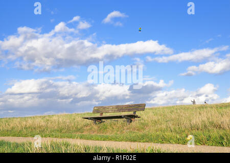 An empty wooden bench on Hampstead Heath with a colourful kite flying in the background Stock Photo