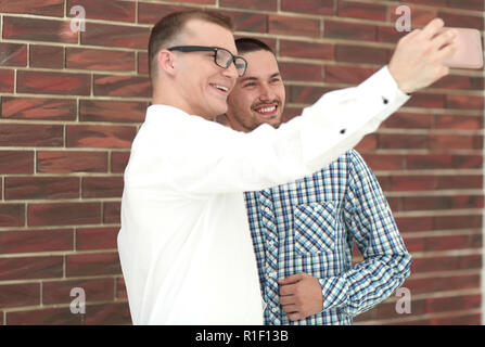 two young men taking selfies standing near a brick wall Stock Photo