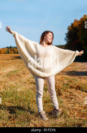 Cheerful girl with raised hands on the field in warm autumn season. Stock Photo