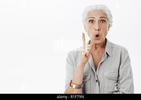 I got excellent advice for daughter. Portrait of excited and enthusiastic creative senior woman with white hair folding lips raising index finger in eureka gesture while having idea adding suggestion Stock Photo