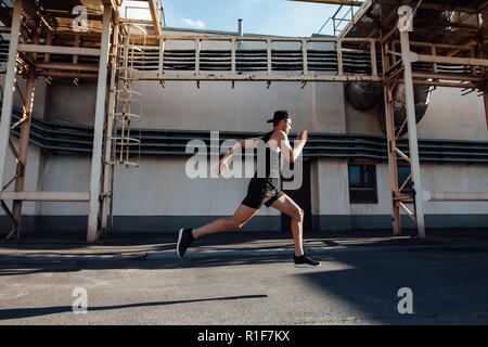 Sporty man running fast in industrial city background. Sport, athletics, fitness, jogging activity Stock Photo