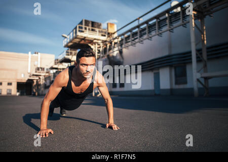 Young serious man doing pushups outdoor on industrial background. concentrated sportsman doing exercise outdoor