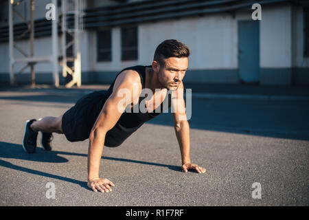 Young serious man doing pushups outdoor on industrial background. concentrated sportsman doing exercise outdoor