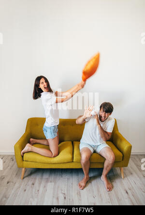 Happy young couple having fun. Woman beating scared boyfriend with pillow on bed. Fighting with pillows. fooling around concept Stock Photo