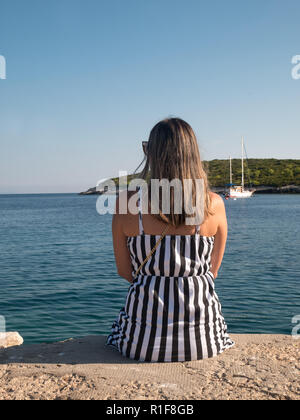 Young woman in black and white dress sitting by the calm Adriatic sea Stock Photo