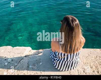 Young woman sitting on stone dock and looking at sea Stock Photo