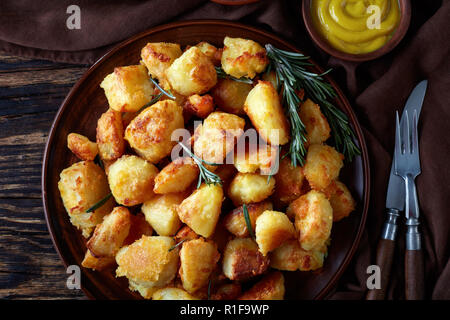 overhead view of crispy Roasted Potatoes with spices and rosemary served on a clay dish with mustard and tomato sauce on an old wooden table, view fro Stock Photo