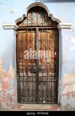 Central American weathered wooden door in a sky blue wall with metal grate covering Stock Photo