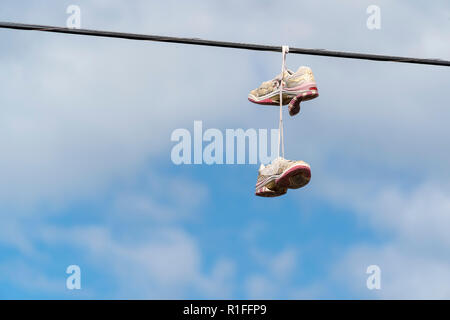 sport shoes hanging on wire cable on blue sky background Stock Photo