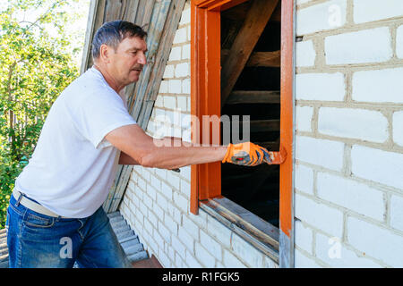 Senior man painting wooden windows using paintbrush. Repairing exterior of old house. Close-up Stock Photo