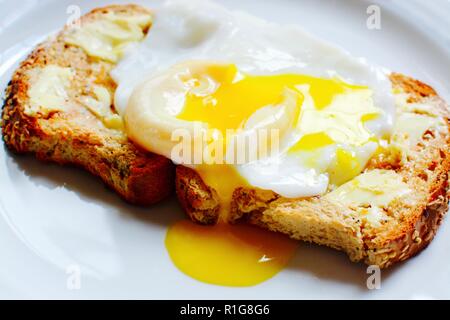 Runny poached egg on brown buttered toast Stock Photo