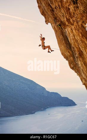 Female rock climber falling of a cliff while lead climbing at sunset Stock Photo