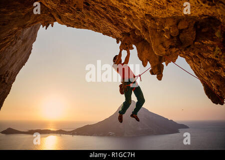 Male rock climber hanging on cliff with one hand at sunset. Kalymnos island,Greece. Stock Photo