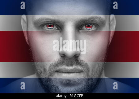 Portrait of a young serious man, in whose eyes the reflected national flag of Costa Rica, against an isolated black background and flag Stock Photo