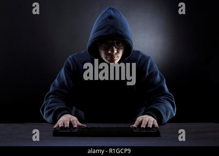 hacker in the hood and glasses in front of a keyboard on a dark background Stock Photo