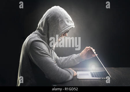 the programmer in the hood and glasses opens the laptop and from there a ray of light, the concept of enlightenment in programming Stock Photo
