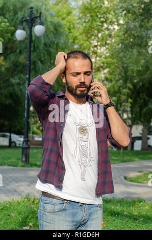 The young man is speaking  at his cell phone at the park. Stock Photo