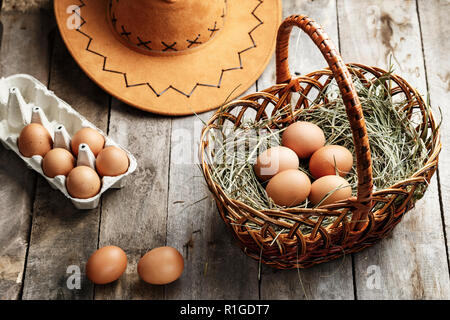 raw chicken eggs in a basket on the table. near the hat and tray. rustic look Stock Photo
