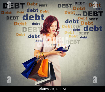 Young woman shopaholic carrying bags holding a empty wallet, shocked about huge debt amount, has no money for shopping in her pouch. Overspending conc Stock Photo