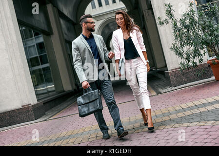 Discussing project. Two young business people walking outside on the city street talking smiling happy man carrying briefcase Stock Photo