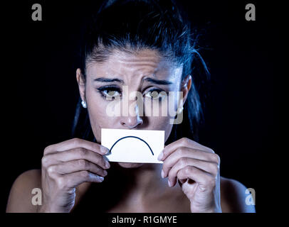 Close up portrait of sad attractive young latin woman suffering from depression in dramatic lighting isolated on black background. Stock Photo