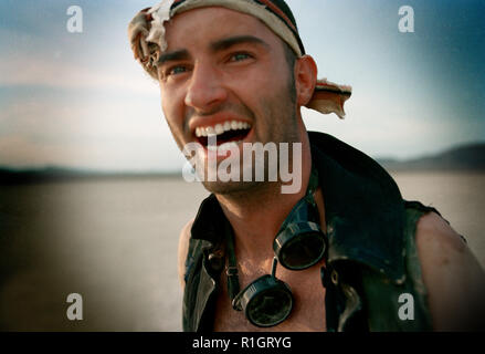 Laughing mid adult man wearing a bandana and goggles around his neck while in a desert. Stock Photo