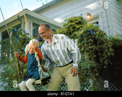 Mature man pushing his daughter on tree swing. Stock Photo