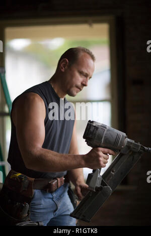 Male builder using a power tool inside a room he is working on. Stock Photo