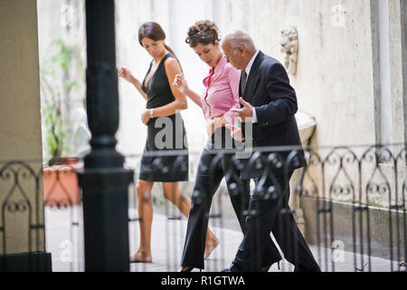 Two mid-adult business woman learning a dance from a senior male colleague in a balcony. Stock Photo