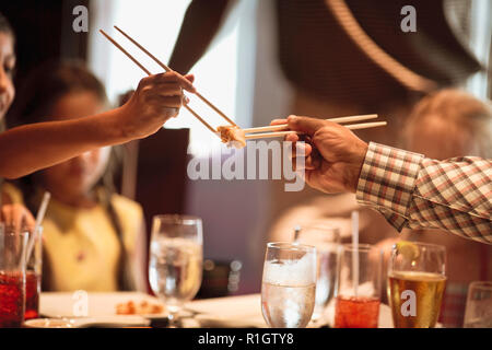 Man handing his daughter a piece of food using chopsticks. Stock Photo