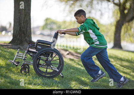 Boy pushing empty wheelchair in a park Stock Photo
