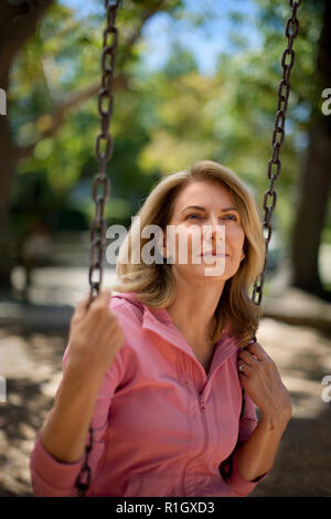 Thoughtful middle aged woman sitting on a swing at the park. Stock Photo