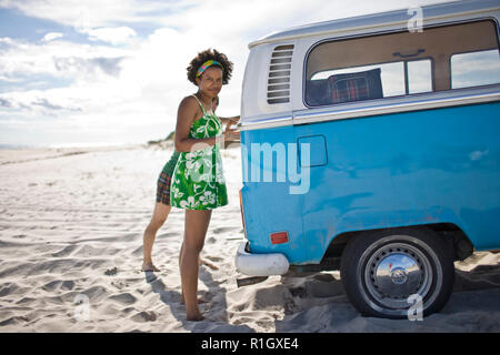 Portrait of a young woman standing next to a van on the beach. Stock Photo